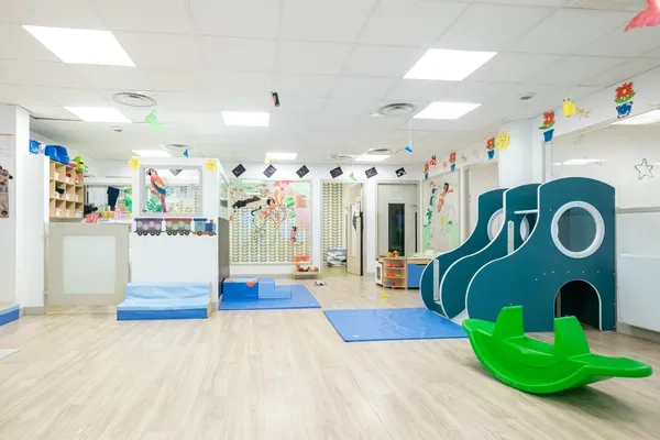 Salle de jeux de la crèche Les Bébés Explorateurs Asnières-sur-Seine Mairie (92600) – structure de motricité bleue marine avec hublot et tunnels, bascule verte, plan incliné mousse bleu et décorations colorées suspendues