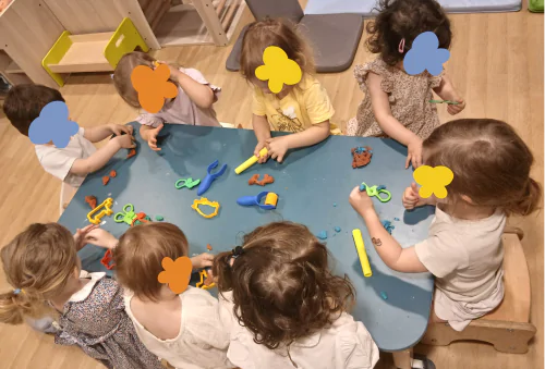 Enfants en crèche à Paris participant à un atelier collectif de pâte à modeler, favorisant la créativité et la socialisation autour d'une activité dirigée.